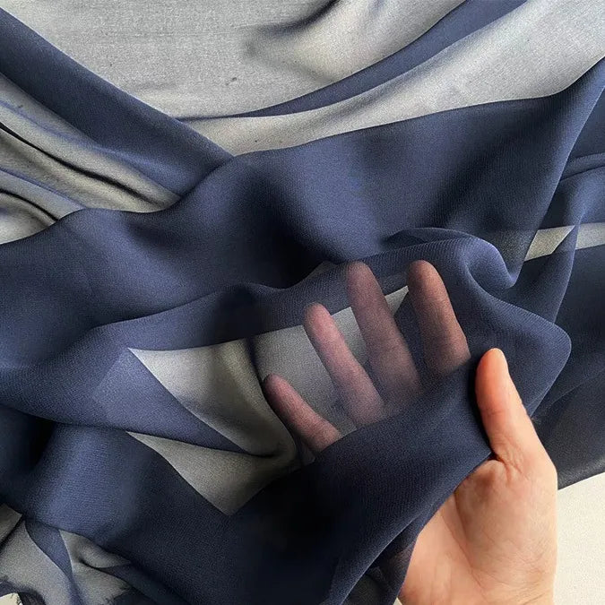 A hand lifts a piece of Longan Craft Georgette Silk Fabric By The Yard, 8 Momme Pure Mulberry Silk Crepe, revealing its soft, sheer texture and semi-transparency as light filters through both the fabric and fingers.