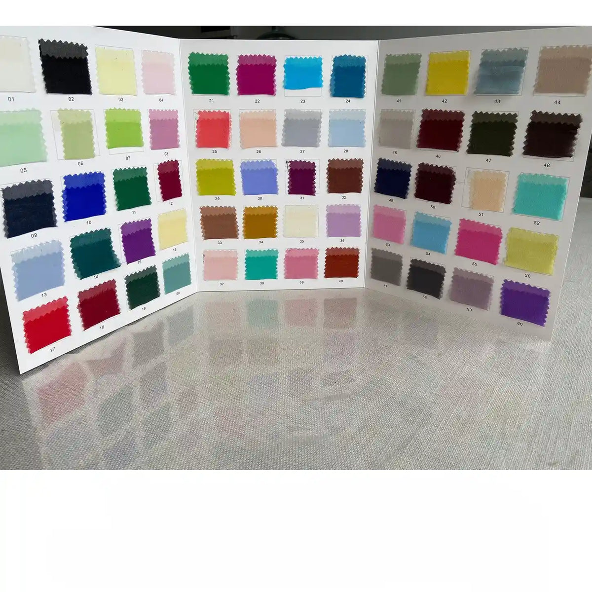A display board with three panels presents colorful Longan Craft Georgette Silk Fabric swatches (8 Momme Pure Mulberry Silk Crepe) in a grid, showcasing a range of vibrant shades across the spectrum on a light, reflective surface.