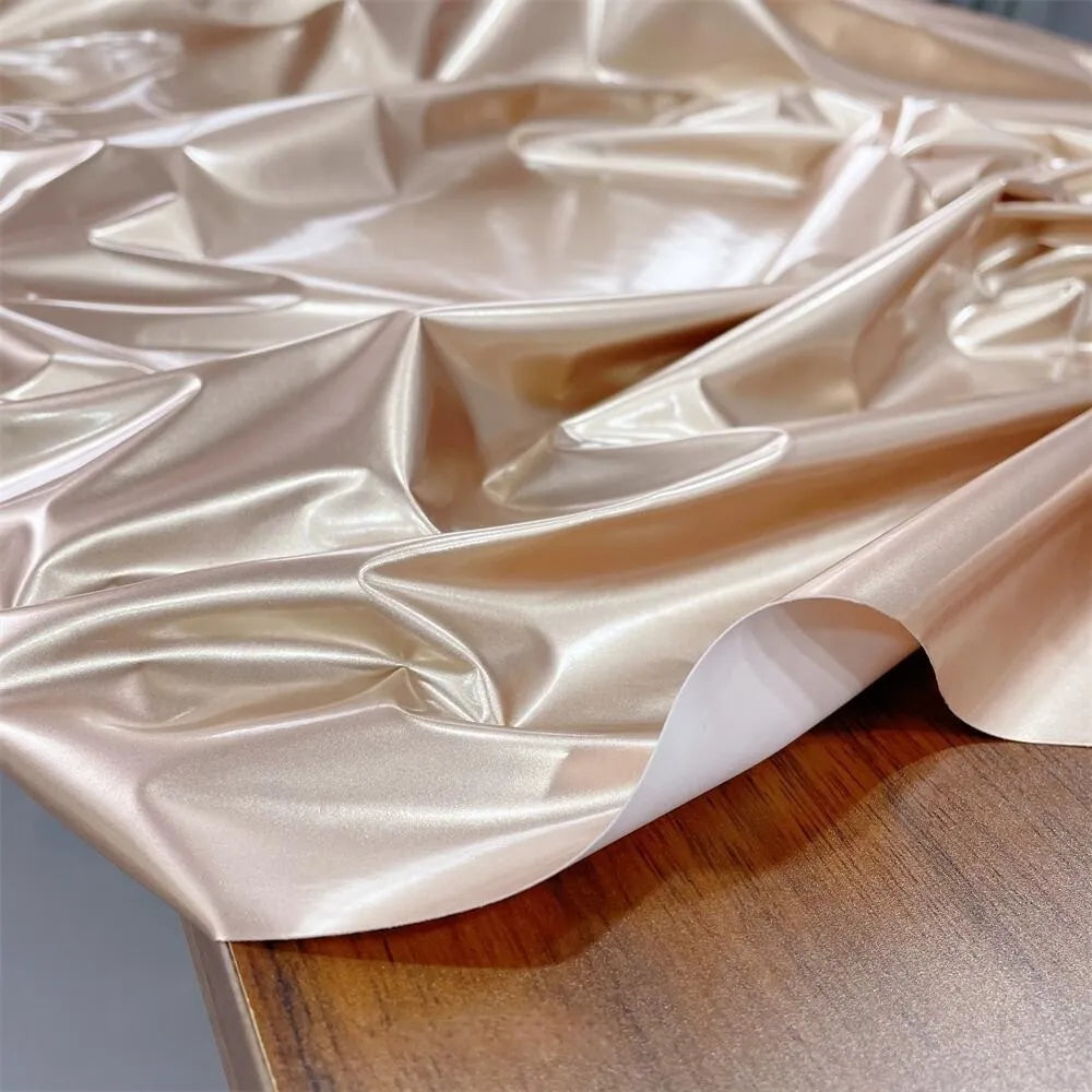 A sheet of Longan Craft Glossy Stretch Vinyl Fabric By The Yard in metallic gold, a shiny PU material ideal for jackets, is displayed with wrinkles on a wooden surface.