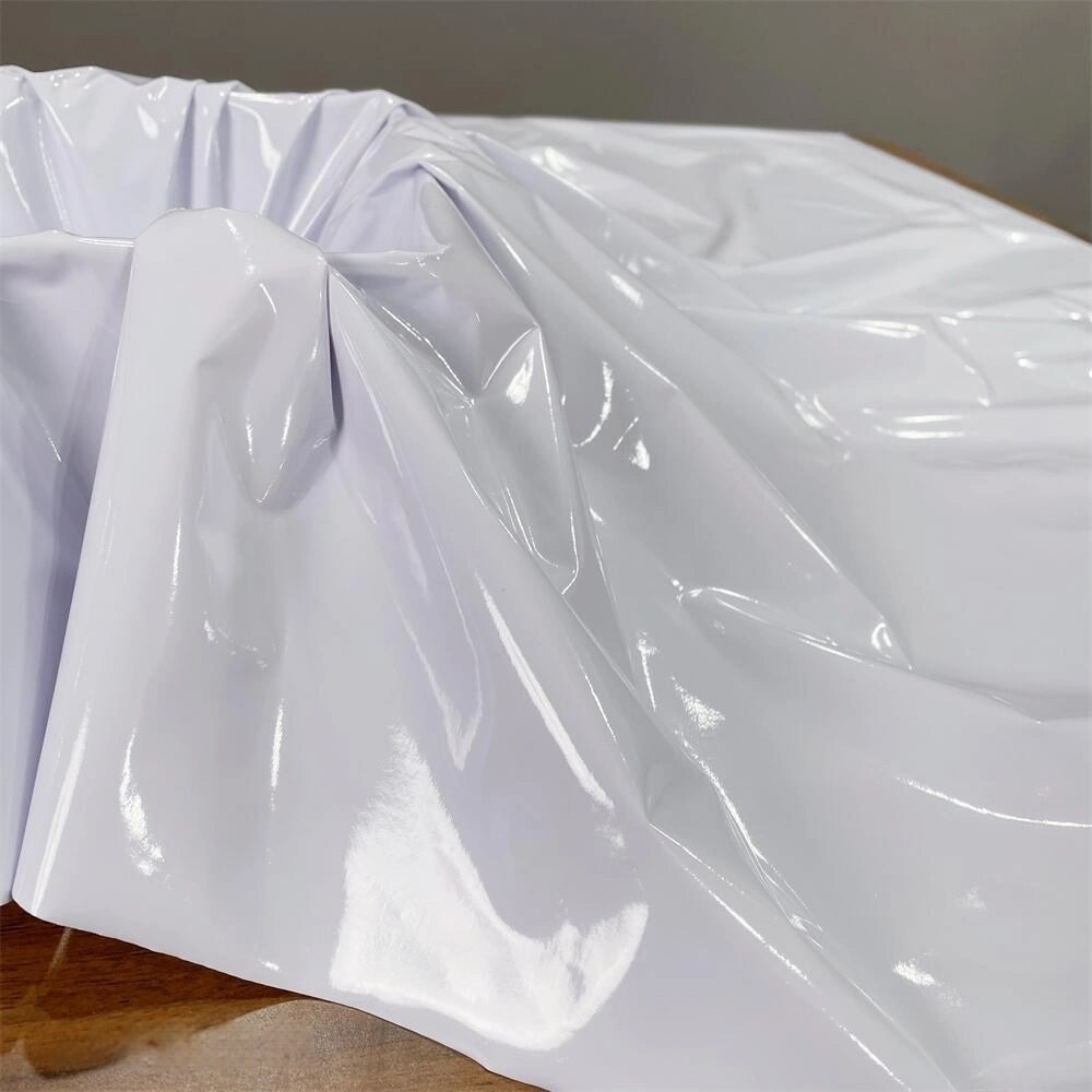 Longan Craft's Glossy Stretch Vinyl Fabric by the Yard, a shiny solid color PU vinyl perfect for jackets, is draped with soft folds over a brown wooden surface, its smooth surface reflecting light.