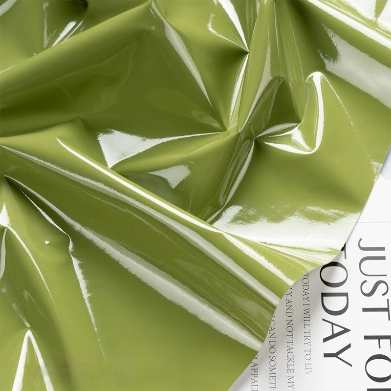 A light green Glossy Stretch Vinyl Fabric By The Yard from Longan Craft, with shiny creases and reflections, drapes over a white page showing the words JUST FOR TODAY. This solid PU vinyl is ideal for making jackets.