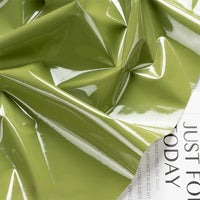 A light green Glossy Stretch Vinyl Fabric By The Yard from Longan Craft, with shiny creases and reflections, drapes over a white page showing the words JUST FOR TODAY. This solid PU vinyl is ideal for making jackets.
