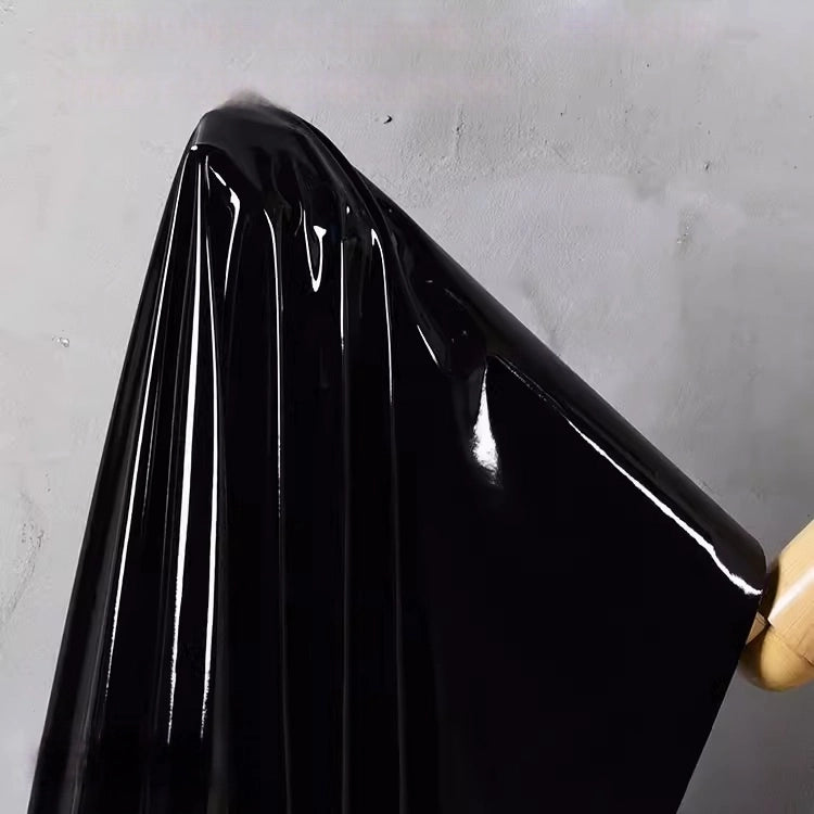 A yard of Longan Craft’s Glossy Stretch Vinyl Fabric in shiny black, with a mirror-like finish and sleek folds, hangs on a wooden hanger against a light gray wall—ideal for jackets.