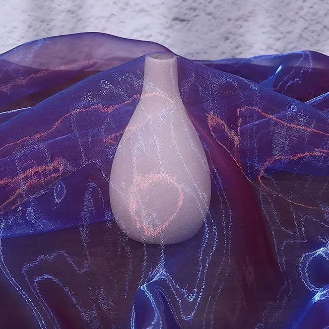 A white ceramic vase sits on a surface, partly covered with Longan Craft Gradient Organza Fabric By The Yard, a lightweight ombre organza. The soft background highlights the elegant effect of this sheer cloth material.