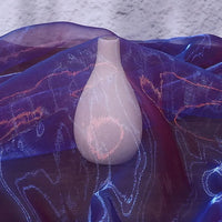 A white ceramic vase sits on a surface, partly covered with Longan Craft Gradient Organza Fabric By The Yard, a lightweight ombre organza. The soft background highlights the elegant effect of this sheer cloth material.