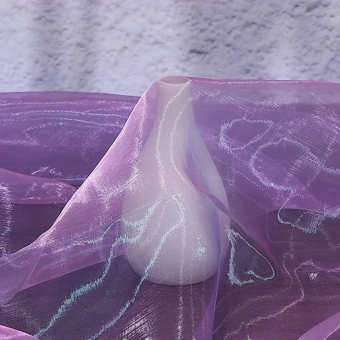 A white vase is partially draped with Longan Craft's Gradient Organza Fabric By The Yard, a lightweight ombre organza material, set against a light textured background.