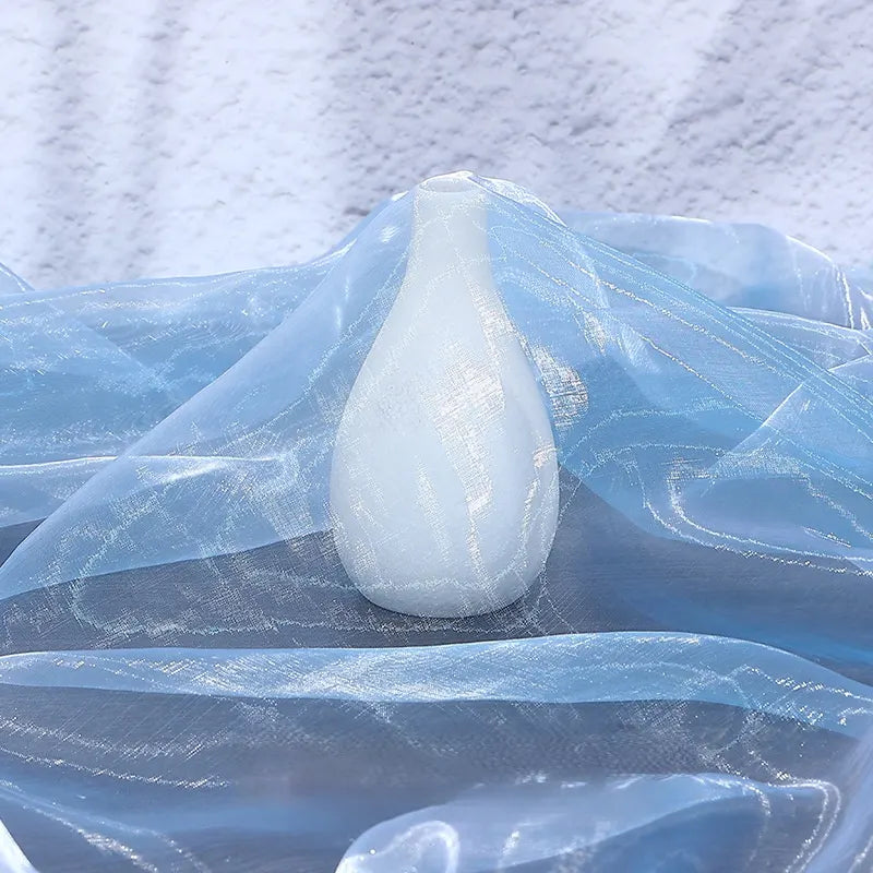 A small white vase is partially wrapped in Longan Craft’s Gradient Organza Fabric By The Yard, a lightweight ombre organza cloth, its sheer shimmer set against a textured white background.