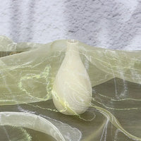 A small, smooth, white vase rests on Longan Craft's lightweight ombre organza fabric, its soft gradient hues evoking bridal elegance against a textured white wall.