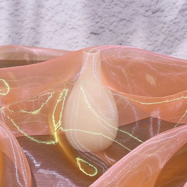 A smooth, light-colored vase draped with Longan Craft’s Gradient Organza Fabric By The Yard—a lightweight, ombre organza cloth—evoking bridal elegance against a textured pale backdrop.