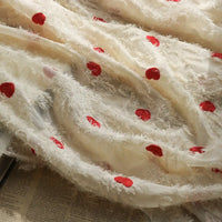 A close-up of Longan craft’s Heart Embroidered Tassel Chiffon Fabric by the yard, a sheer jacquard fabric with fluffy details and red dots, draped over an open newspaper—ideal sewing material for spring and summer women’s dresses.