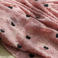 A close-up of Longan craft's Heart Embroidered Tassel Chiffon Fabric by the yard, featuring textured fuzzy hearts and black heart patterns, draped over a surface with faint text beneath—ideal Jacquard fabric for spring and summer dresses.
