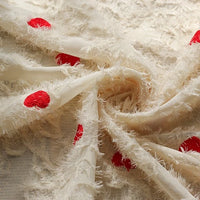 Close-up of Longan craft's Heart Embroidered Tassel Chiffon Fabric by the yard, a cream jacquard material with red heart embroidery and a fringe-like texture, softly draped—ideal for spring and summer women’s dresses.