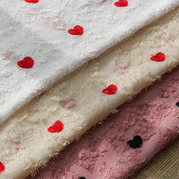 Three layers of Longan craft Heart Embroidered Tassel Chiffon Fabric by the yard—white, cream, and pink with red and black heart embroidery—are stacked on a printed surface; ideal for spring/summer women’s dress sewing.