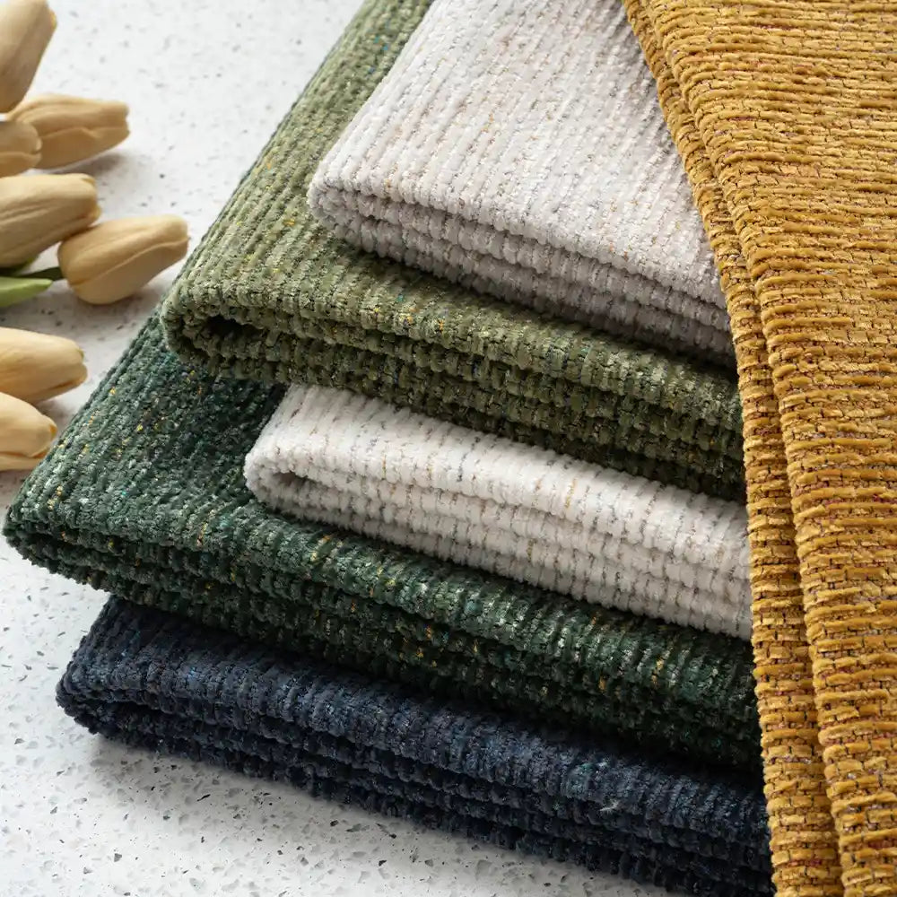 A neatly stacked pile of ribbed towels in yellow, green, white, dark green, and navy blue rests by beige tulips, echoing the cozy vibe of Longan Craft’s Heavy Weight Slub Chenille Fabric—premium upholstery material by the yard.