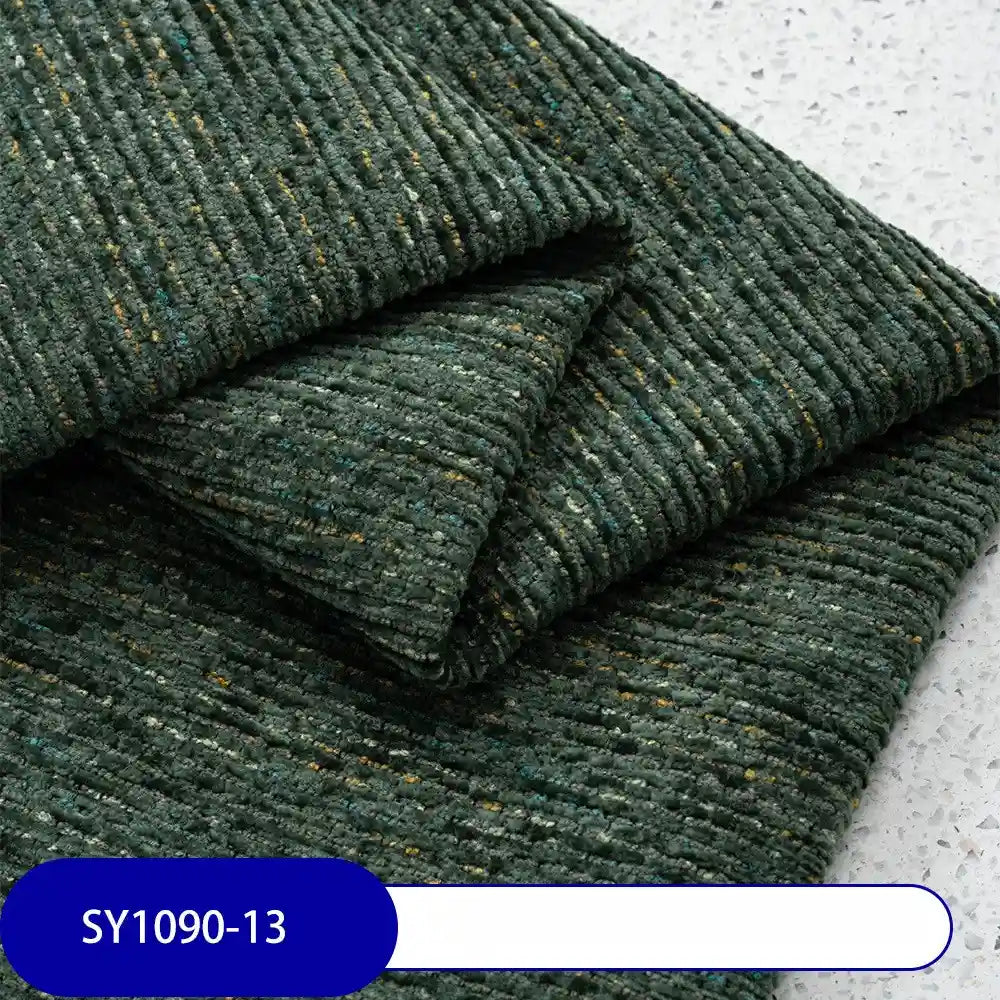Folded dark green Heavy Weight Slub Chenille Fabric by Longan Craft, with yellow and blue flecks, sits on a light speckled surface. A blue label shows SY1090-13. Premium thick polyester chenille adds multicolor style to any upholstery project.