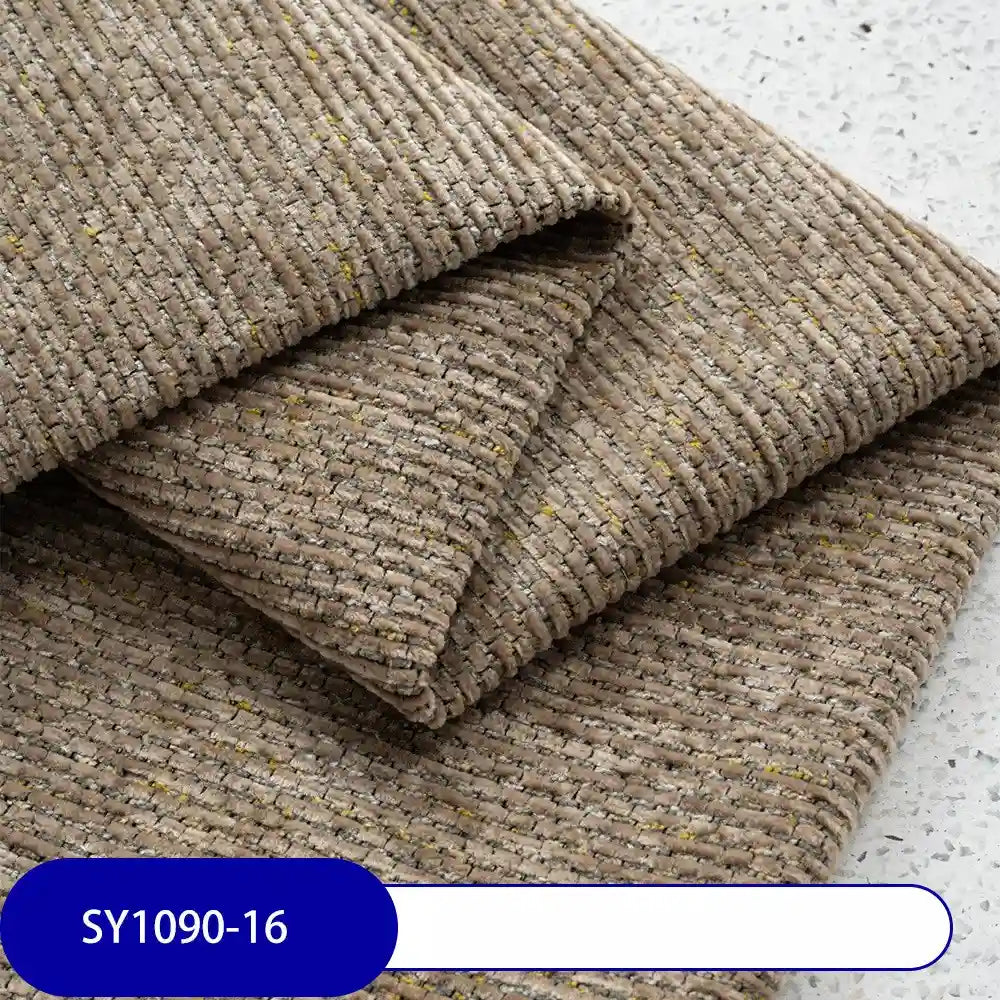 Close-up of folded, textured beige-brown Heavy Weight Slub Chenille Fabric By The Yard from Longan Craft, with subtle yellow flecks. Thick polyester chenille material shown on a speckled surface; blue and white SY1090-16 label visible.