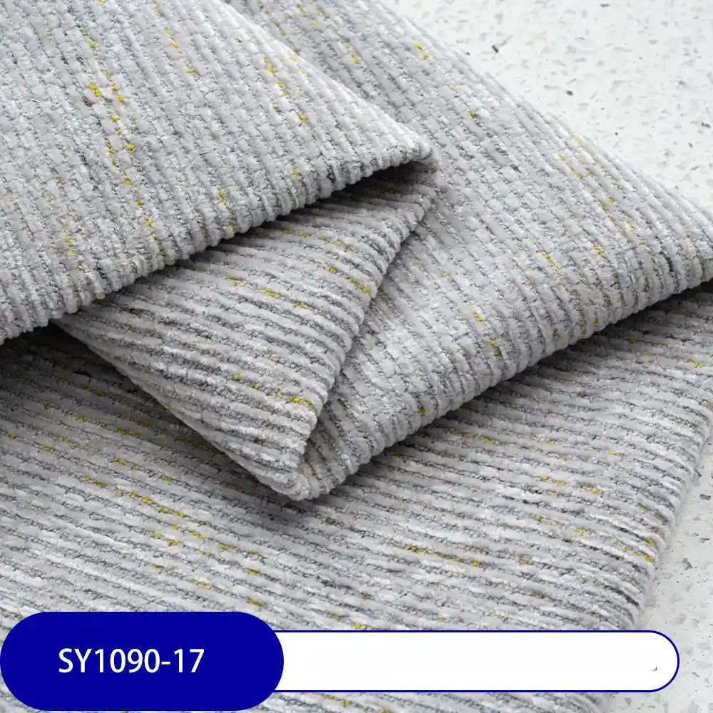 A folded piece of Longan Craft Heavy Weight Slub Chenille Fabric By The Yard in light gray with yellow flecks is shown on a flat surface. The thick, textured polyester upholstery fabric features a SY1090-17 label in white on blue.