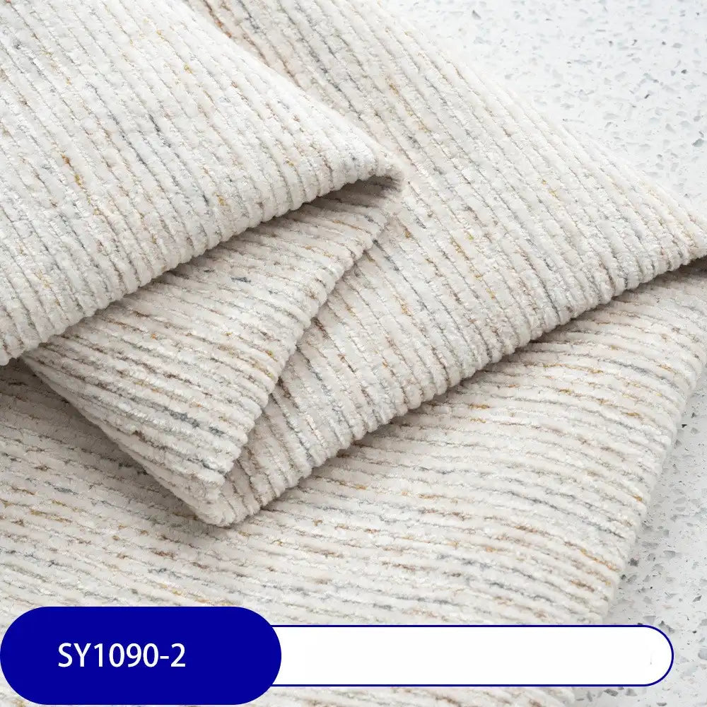 A close-up of Longan Craft's Heavy Weight Slub Chenille Upholstery Fabric shows folded, cream-colored polyester with subtle gray and beige speckles, ribbed texture, and a “SY1090-2” blue label in the corner.
