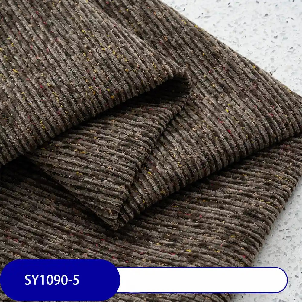Heavy Weight Slub Chenille Fabric by Longan Craft is shown folded, with brown ribbed heathered flecks and subtle red-yellow specks, resting on a light speckled surface. Blue label at bottom left: SY1090-5.