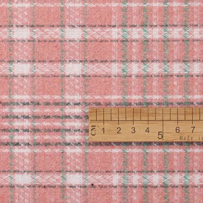 A wooden ruler displaying measurements from 0 to 10 centimeters rests on Longan Craft’s Heavyweight Cotton Checked Flannel Fabric by the Yard, a vintage fall winter polyester brushed mammoth flannel material featuring a pink plaid pattern with white, green, and gray lines.