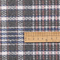 A wooden ruler measures a piece of Longan Craft’s Heavyweight Cotton Checked Flannel Fabric, featuring a grey, white, red, and blue pattern. The ruler is placed horizontally across the polyester brushed Mammoth flannel clothing material and indicates a length from 1 to 8 centimeters.