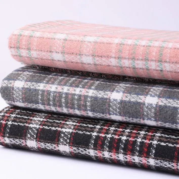 A stack of three folded pieces of Longan Craft Heavyweight Cotton Checked Flannel Fabric is shown: the top features a light pink plaid, the middle is gray plaid, and the bottom displays a black plaid accented with red and white lines. Each piece is made from soft, heavyweight cotton flannel—perfect for cozy garments or home projects—as part of the Polyester Brushed Mammoth Flannel Clothing Material collection, ideal for vintage fall and winter creations.