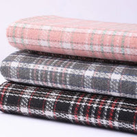 A stack of three folded pieces of Longan Craft Heavyweight Cotton Checked Flannel Fabric is shown: the top features a light pink plaid, the middle is gray plaid, and the bottom displays a black plaid accented with red and white lines. Each piece is made from soft, heavyweight cotton flannel—perfect for cozy garments or home projects—as part of the Polyester Brushed Mammoth Flannel Clothing Material collection, ideal for vintage fall and winter creations.