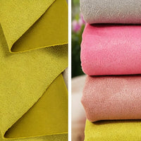 Close-up of Longan Craft’s Heavyweight Microfiber Faux Suede Fabric By The Yard: on the left, a folded yellow soft imitation suede; on the right, a stack of folded multicolor brushed microsuede materials in gray, pink, brown, and beige—ideal upholstery fabric for adding a luxurious touch to your DIY clothing projects.