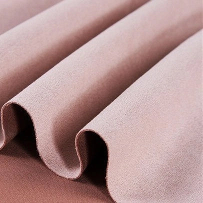 Close-up of the Longan Craft Heavyweight Microfiber Faux Suede Fabric by the Yard, shown in light pink and draped in soft, smooth folds that create gentle wavy lines and shadows. The multicolor brushed microsuede material appears velvety with a soft-to-the-touch texture—ideal for DIY clothing projects.