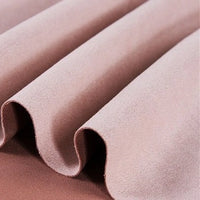 Close-up of the Longan Craft Heavyweight Microfiber Faux Suede Fabric by the Yard, shown in light pink and draped in soft, smooth folds that create gentle wavy lines and shadows. The multicolor brushed microsuede material appears velvety with a soft-to-the-touch texture—ideal for DIY clothing projects.