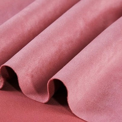 Close-up of Longan Craft Heavyweight Microfiber Faux Suede Fabric by the yard in a soft pink shade, draped in gentle folds to showcase its smooth and luxurious multicolor brushed microsuede texture—perfect for DIY clothing projects.