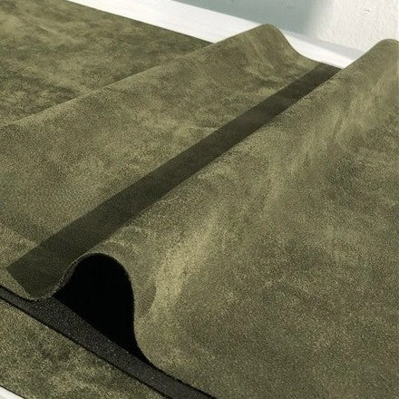 A close-up of the Longan Craft Heavyweight Microfiber Faux Suede Fabric by the yard in olive green, featuring a textured, brushed microsuede surface with a wavy, folded section running diagonally across the soft imitation suede material.