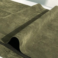 A close-up of the Longan Craft Heavyweight Microfiber Faux Suede Fabric by the yard in olive green, featuring a textured, brushed microsuede surface with a wavy, folded section running diagonally across the soft imitation suede material.