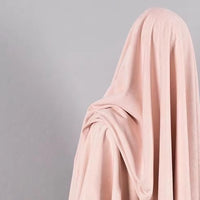 A person is fully draped in Longan Craft’s Heavyweight Microfiber Faux Suede Fabric—a soft, pale pink imitation suede ideal for DIY clothing projects—concealing their face and body against a plain gray background.