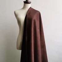 A dressmaker’s mannequin is draped with a large piece of Longan Craft Heavyweight Microfiber Faux Suede Fabric in brown, its smooth, soft surface elegantly falling over one shoulder against a plain white background.