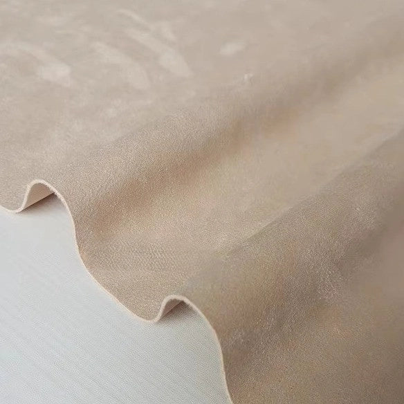 A close-up of a sheet of Longan Craft Heavyweight Microfiber Faux Suede Fabric By The Yard in light beige, draped in gentle waves to display its soft texture and smooth, brushed microsuede surface—perfect as an elegant upholstery or DIY clothing fabric.