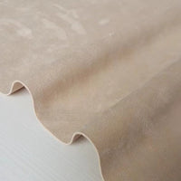 A close-up of a sheet of Longan Craft Heavyweight Microfiber Faux Suede Fabric By The Yard in light beige, draped in gentle waves to display its soft texture and smooth, brushed microsuede surface—perfect as an elegant upholstery or DIY clothing fabric.