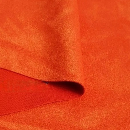 A close-up of a piece of Longan Craft Heavyweight Microfiber Faux Suede Fabric By The Yard in bright orange, folded to display its soft, smooth, and slightly shiny texture—perfect for DIY clothing projects.