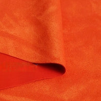 A close-up of a piece of Longan Craft Heavyweight Microfiber Faux Suede Fabric By The Yard in bright orange, folded to display its soft, smooth, and slightly shiny texture—perfect for DIY clothing projects.