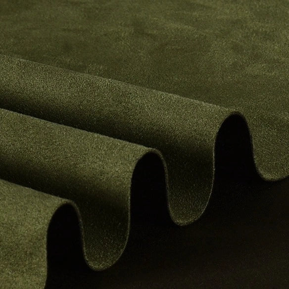 Close-up of the Longan Craft Heavyweight Microfiber Faux Suede Fabric by the Yard, with multicolor brushed microsuede draped in smooth, rounded waves against a dark background—showcasing its soft texture and rich green hue. This soft imitation suede material is an ideal choice for DIY clothing projects.
