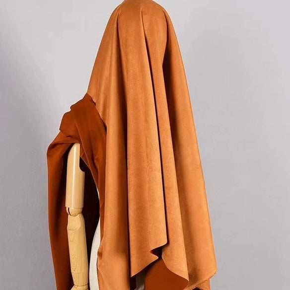 A wooden mannequin is draped in Longan Craft’s Heavyweight Microfiber Faux Suede Fabric By The Yard, in a rich brown shade, completely covering its upper body and head to create a ghost-like silhouette against a plain gray background. The soft, brushed microsuede material lends depth and texture to the scene.