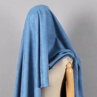 A wooden mannequin is draped in Longan Craft’s Heavyweight Microfiber Faux Suede Fabric By The Yard—shown here in a blue brushed microsuede—concealing its head and upper body against a plain gray backdrop.