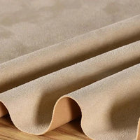 A close-up of Longan Craft’s Heavyweight Microfiber Faux Suede Fabric by the yard in beige, featuring soft, multicolor brushed microsuede material draped in smooth, gentle waves on a wooden surface—perfect for DIY clothing projects.