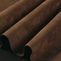 A close-up of folded Longan Craft Heavyweight Microfiber Faux Suede Fabric by the Yard showcases its soft, velvety microfiber surface in rich brown, with gentle waves and shadows highlighting the luxurious brushed texture—ideal for DIY clothing projects.