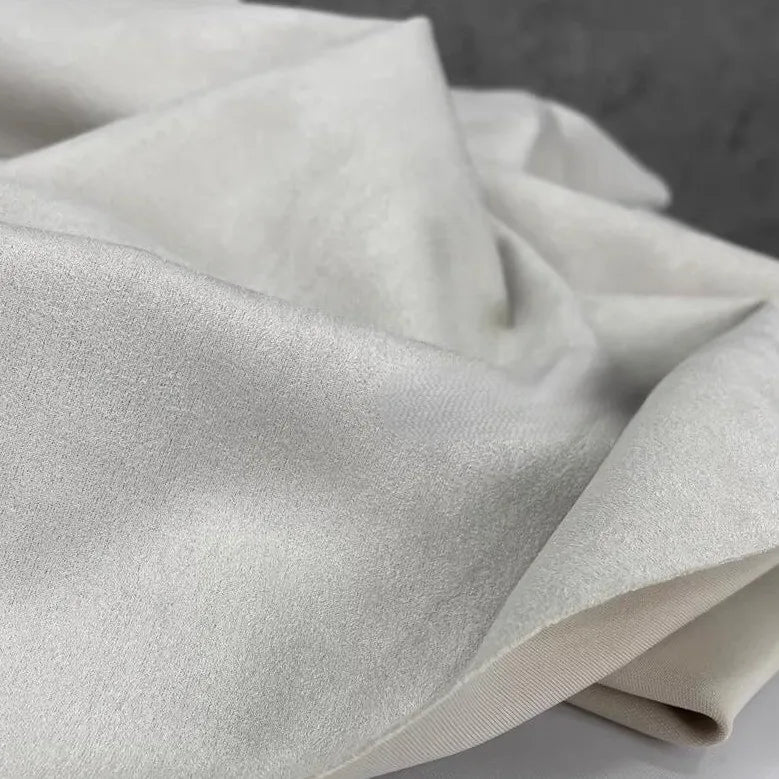 Experience a close-up of Longan Craft’s Heavyweight Microfiber Faux Suede Fabric By The Yard, featuring soft, white multicolor brushed microsuede material with a slightly shiny finish, draped and folded to highlight its smooth, elegant surface and delicate sheen—perfect for DIY clothing projects.