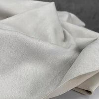 Experience a close-up of Longan Craft’s Heavyweight Microfiber Faux Suede Fabric By The Yard, featuring soft, white multicolor brushed microsuede material with a slightly shiny finish, draped and folded to highlight its smooth, elegant surface and delicate sheen—perfect for DIY clothing projects.