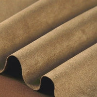 A close-up of Longan Craft’s Heavyweight Microfiber Faux Suede Fabric By The Yard showcases its light brown, multicolor brushed microsuede material, folded in soft, even waves to display its smooth, velvety texture and elegant matte finish—perfect for DIY clothing projects with a luxurious suede look.