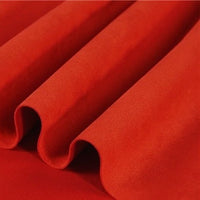 Close-up of folded red Longan Craft Heavyweight Microfiber Faux Suede Fabric By The Yard, featuring a smooth, soft texture that forms gentle waves and shadows—ideal for DIY clothing projects.