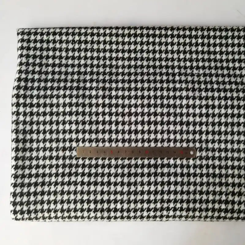 A piece of Longan Craft Houndstooth Mammoth Flannel Fabric by the yard is laid flat with a metal ruler on top, displaying the scale of its black and white pattern on a plain white background.