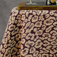 A close-up of Longan Craft’s Leopard Embossed Brocade Fabric By The Yard, a stretch jacquard brocade with beige and brown leopard print, draped on a table and featuring part of a vintage sewing machine in the corner.